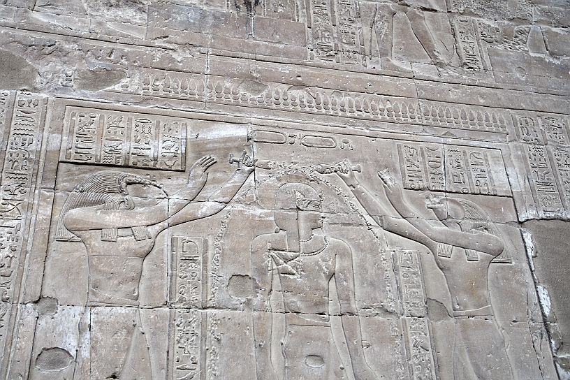 12 MAK_6261.jpg - A sinistra il dio Horus, con la testa di falco, signore del tempio, a destra il dio Thot, raffigurato con la testa di ibis, dio della saggezza e della scrittura. I flussi d'acqua sono spesso rappresentati da una catena di simboli ankh (vita) e was (potere), a simboleggiare che il re viene lavato con la vita e la forza divina.